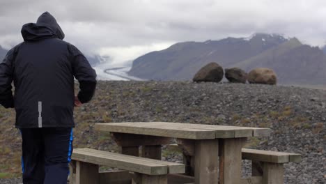 man walking to picnic table with glacier in background