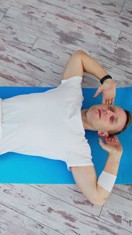 man training at home. keeping fit. young man in white t-shirt and black pants doing workout on a mat. sport and health. top view.. vertical video