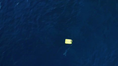 yellow gas tank and weathered rope flotsam debris floats in ocean, aerial static top down perspective