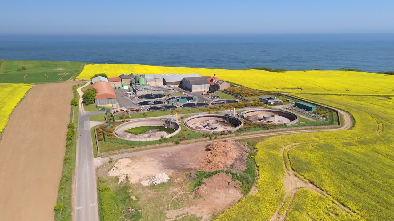 Aerial drone view of a wastewater treatment plant in a bright yellow rapeseed field on a sunny summer day in North Yorkshire, UK