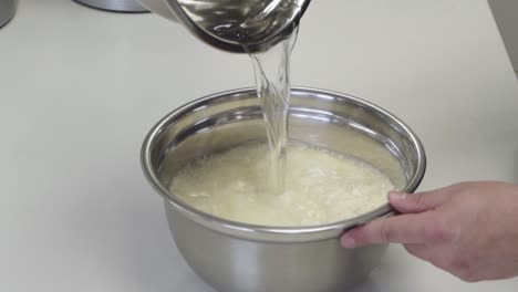 primer plano de agregar agua a la harina mientras se hace masa de pan fresco