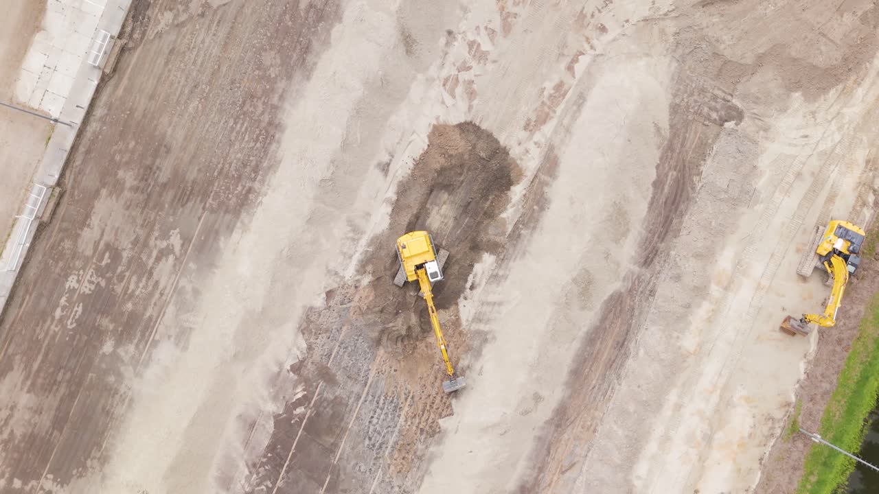 Close aerial shot of a yellow excavator moving and leveling soil as part of a football field renovation