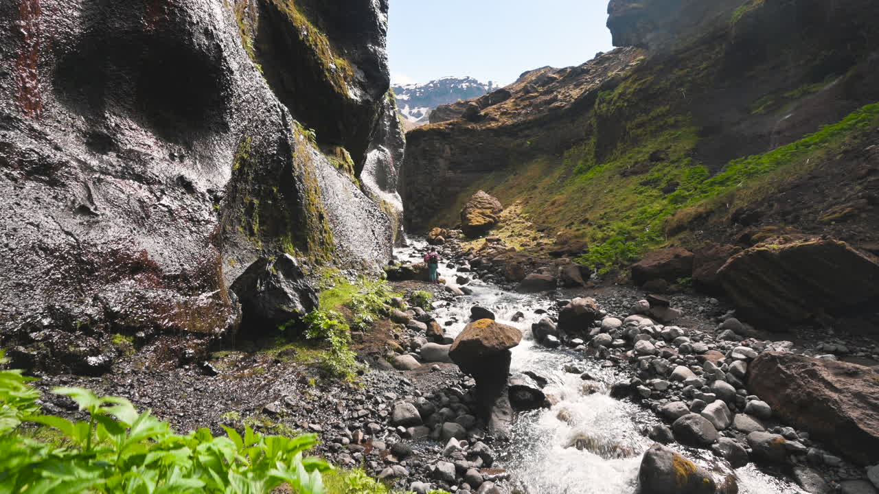 hojas verdes que revelan a un excursionista a lo lejos caminando a lo largo de un río al fondo de un cañón en las montañas