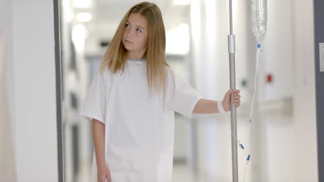 caucasian girl patient walking with drip stand in hospital corridor, slow motion