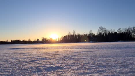 Wind-blowing-over-snowy-surface-in-midwinter-landscape-at-sunset,-Northern-Finland