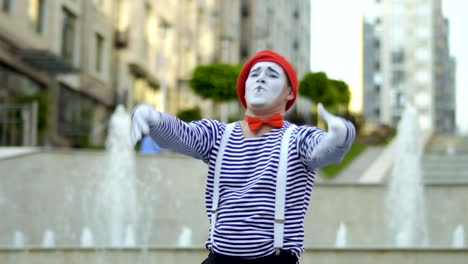 funny mime in red beret gesticulate hands at fountains background