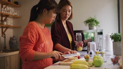 Asian-mother-and-daughter-preparing-healthy-drink-in-kitchen-smiling