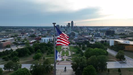 american flag and iowa state flag waving in front of capital city, des moines, ia