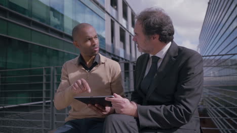 Male-managers-having-discussion-with-tablet-near-office-building