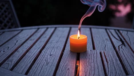 burning candle on wooden patio table at dusk