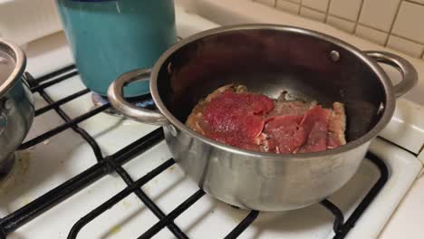 beef steaks cooked in steel pot on gas stove.