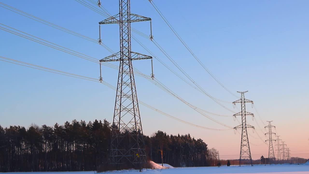 Winter evening pan across high voltage transmission towers stretching over snow covered farmland under warm sunset sky