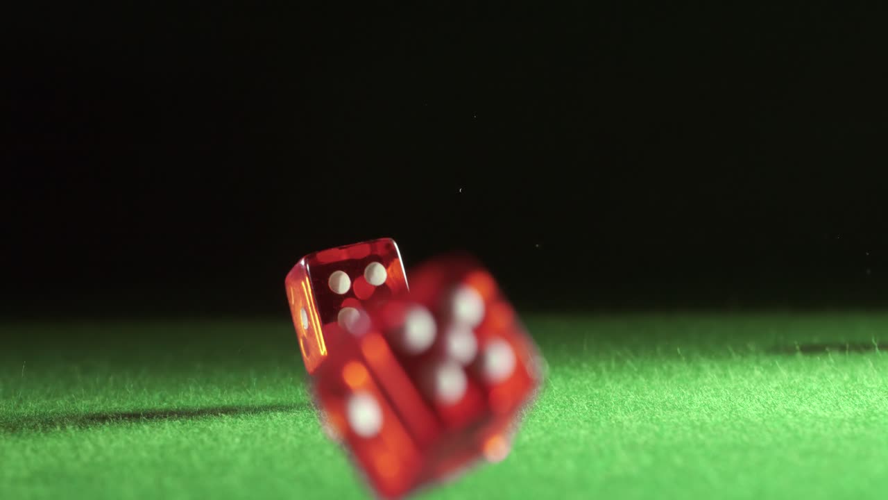 Red dice falling and bouncing on green table on a dark background. Shot on super slow motion camera 1000 fps