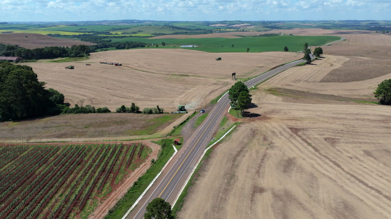 Harvested farmland aerial with rural road and harvest machines operating