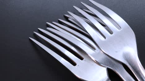 detail shot of four steel forks face down on a black bacground, rotating motion