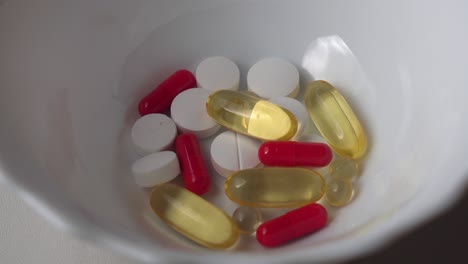 different color vitamin pills and capsules fall into ceramic container