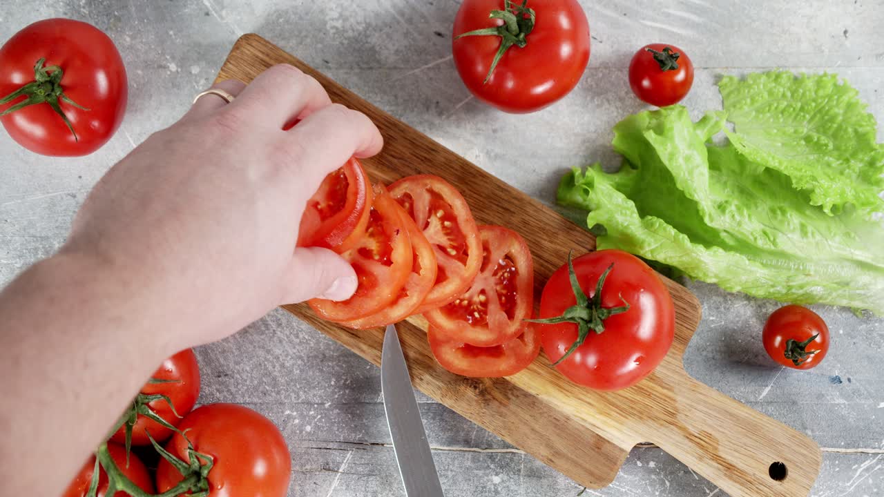 남성 손은 절단판에 토마토 조각을 놓았습니다.