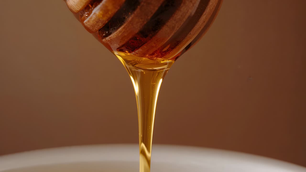Mestolo per miele in legno scanalato inclinato che rilascia un flusso di miele dorato in una ciotola bianca poco profonda per amalgamarsi
