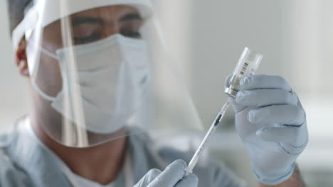 doctor in protective uniform drawing vaccine out with syringe