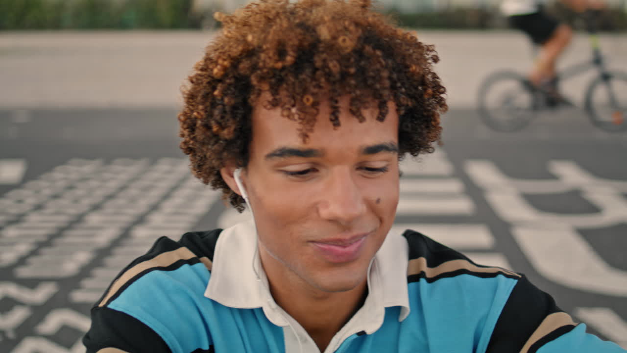 Adolescent joyeux prenant un selfie en pleine rue, gros plan. Jeune avec écouteurs utilisant son smartphone.