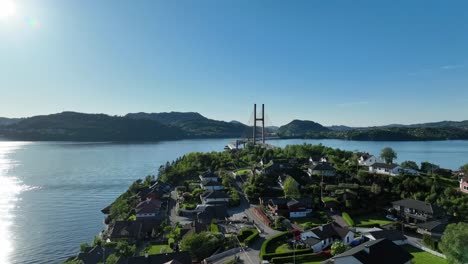 Residential-area-at-Tellevik-and-Hordvik-with-fjord-and-Nordhordland-bridge-in-background,-Summer-aerial