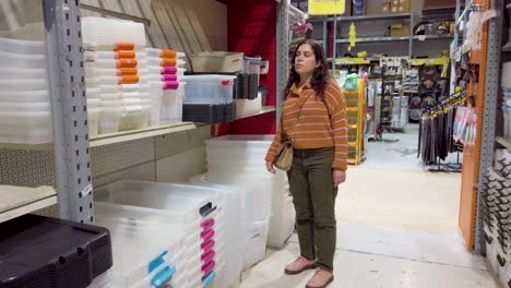 a woman is shopping in a store and looking at a shelf of plastic containers