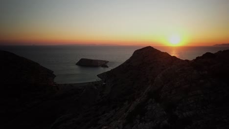 drone push past rocky outcropping to syros greece overlook, stunning golden glow sunset