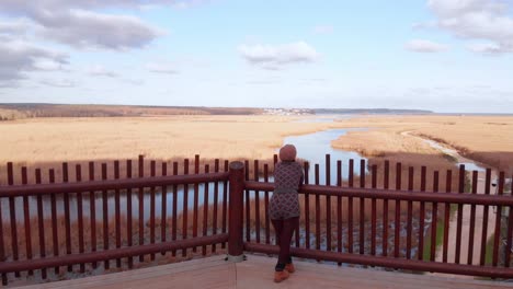 girl-walking-towards-view-at-bird-watching-point,-drone-going-forward,-aerial-shot