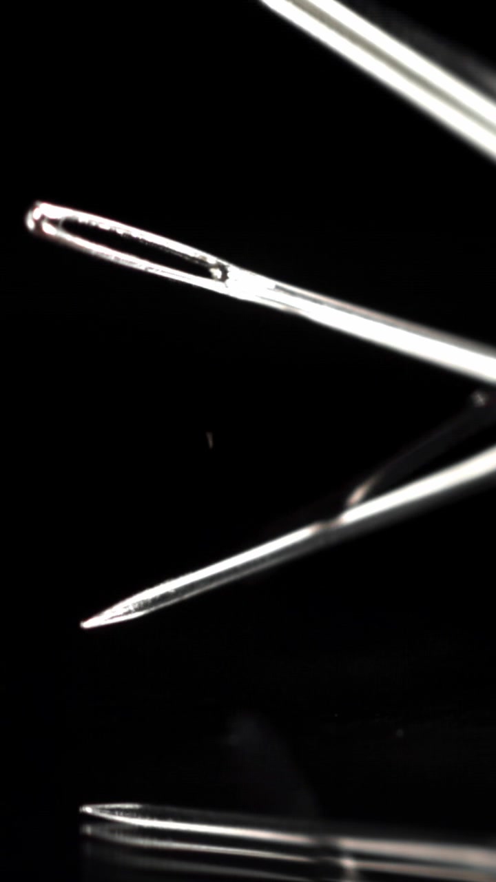 Shiny Metal Sewing Needles Falling in Slow Motion on a Black Background