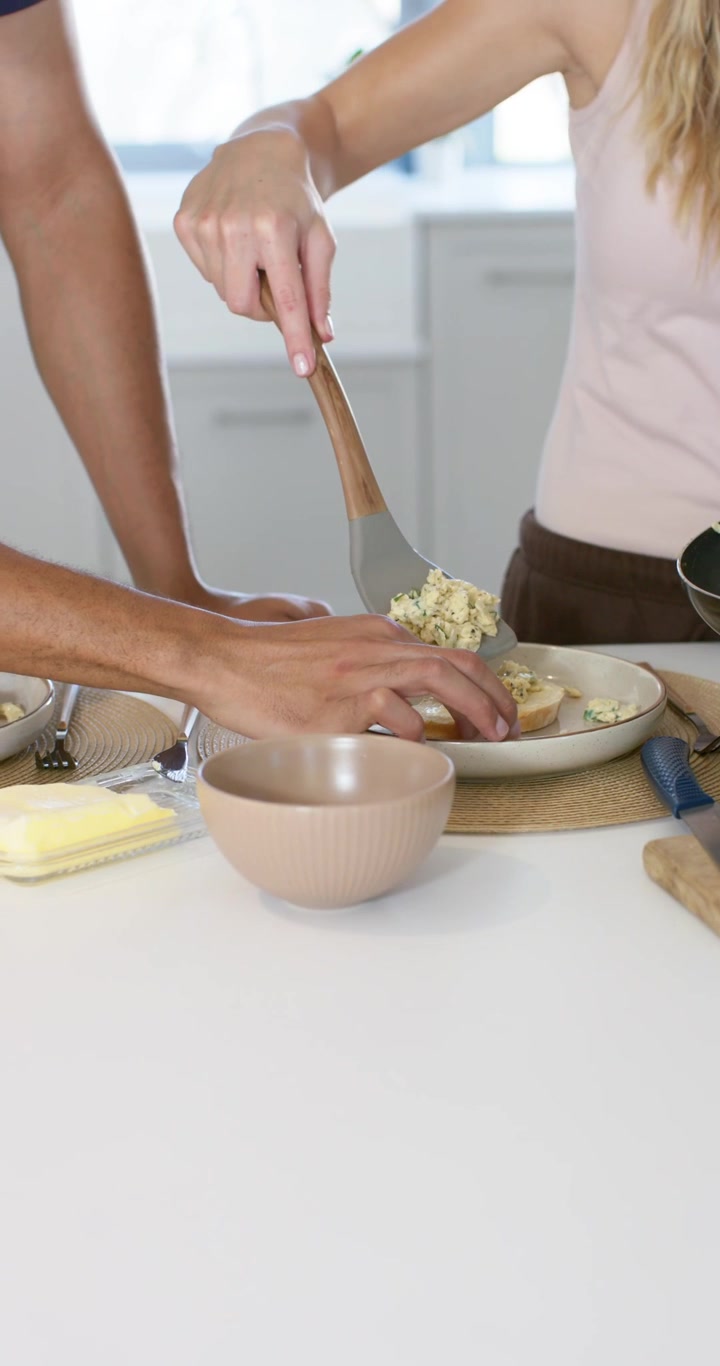Video verticale: Coppia che prepara il brunch sul bancone, l'uomo che porge un piatto e la donna che raccoglie le uova con una spatola