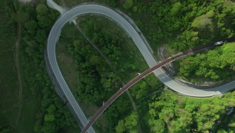 static aerial overhead view of a winding road intersected by an old railway bridge in the middle of a forest