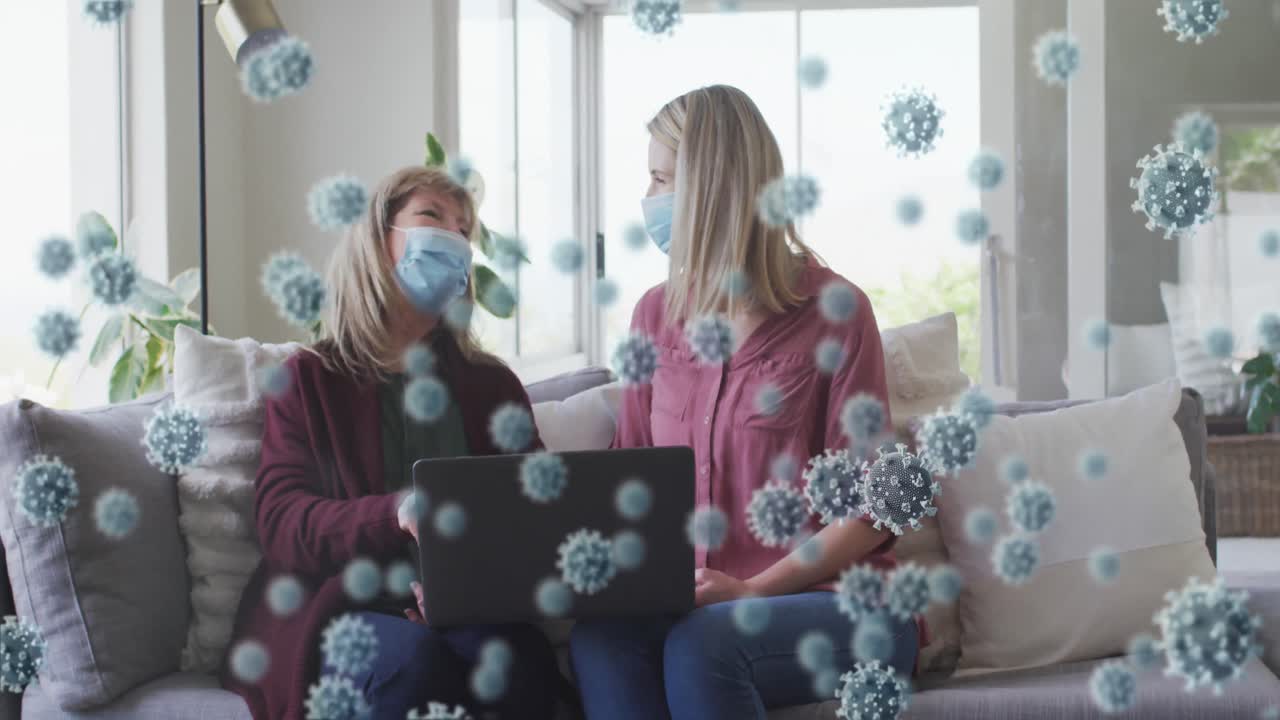 animación de células del virus covid 19 sobre mujeres mayores caucásicas felices que usan máscaras faciales usando una computadora portátil