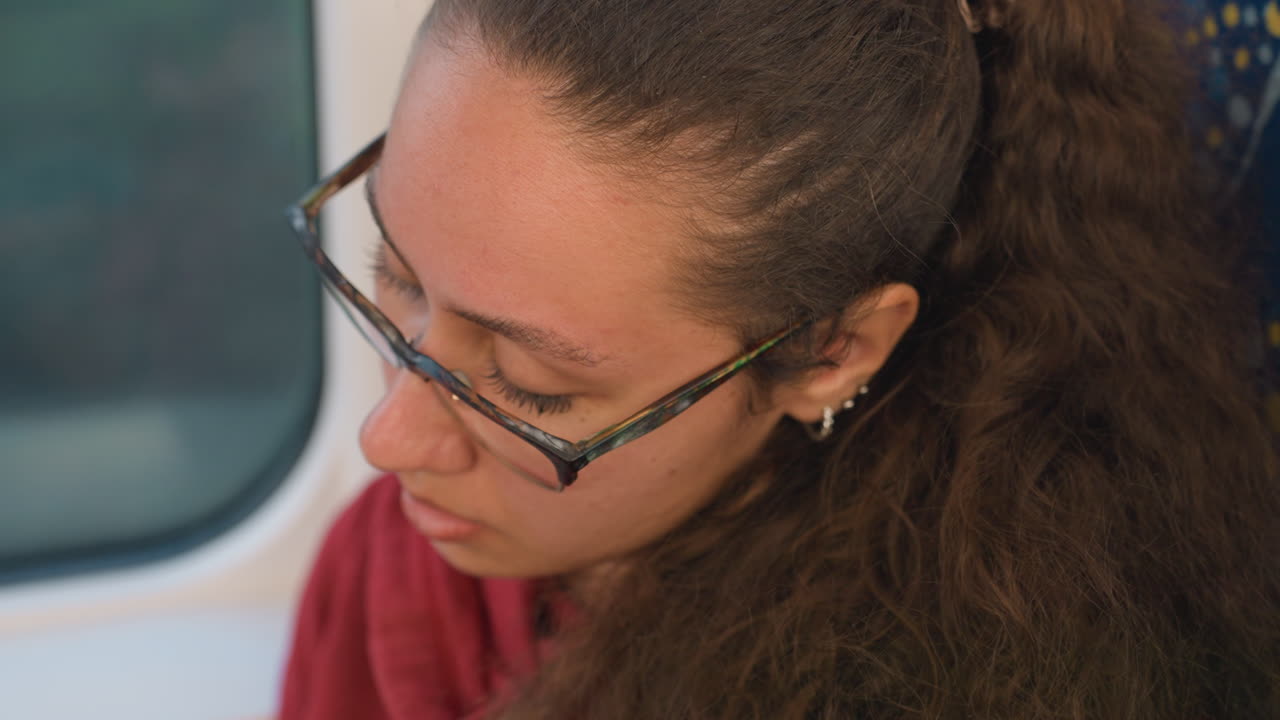 Donna in treno mostra un'emozione sottile. Passeggero con capelli ricci comunica con un sussurro delicato. Giovane donna con occhiali esibisce sentimenti introspettivi durante un faticoso viaggio in treno