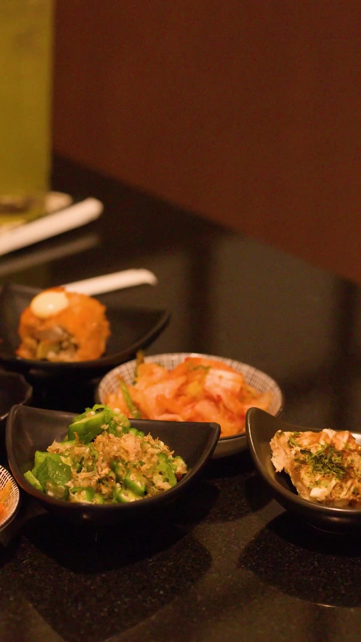 Close-up of hand placing a small sauce dish among various Japanese appetizers in an izakaya.