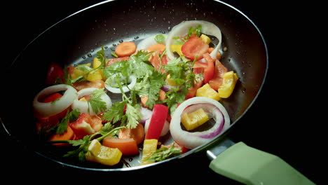 slow rotating frying pan full of chopped vegetables on black background