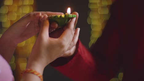 close up of man handing lit diya oil lamp to woman celebrating festival of diwali