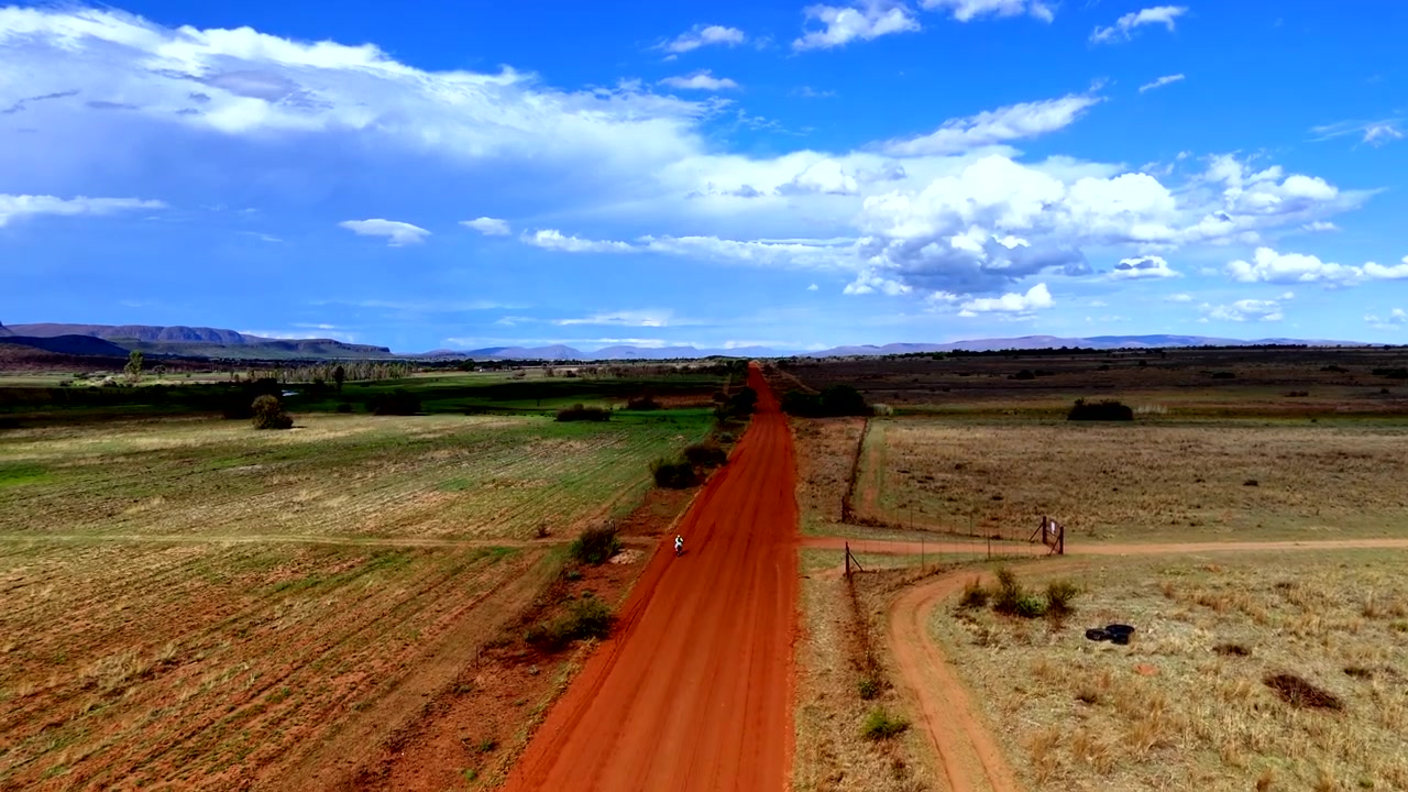 Abitante locale in bicicletta su una strada sterrata rossa rurale in un paesaggio africano, vista aerea
