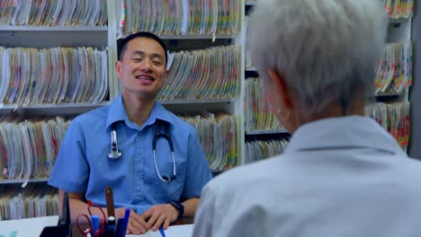 Young-Asian-male-doctor-and-senior-patient-interacting-with-each-other-at-clinic-4k