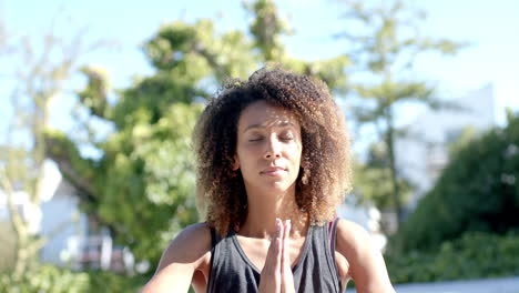 Happy-biracial-woman-practicing-yoga-meditation-sitting-in-sunny-garden,-slow-motion