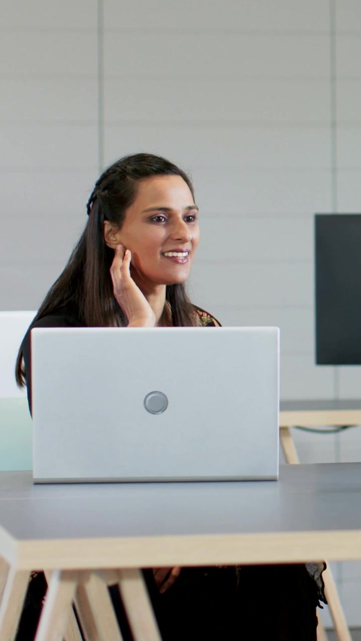 Video verticale: Donna sorridente che guarda a destra e parla in ufficio, enfatizzando le idee con un laptop.