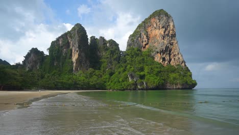 small waves crashing on railay beach, krabi thailand with giant cliffs next to ocean - cloudy morning