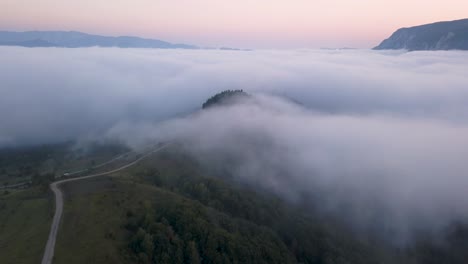 aerial footage showing a hill surrounded by a valley covered in fog