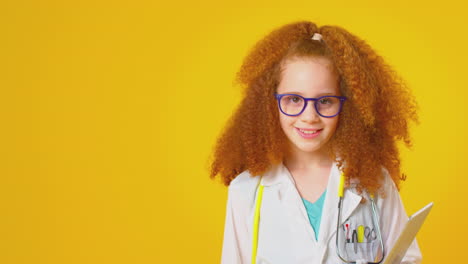 studio portrait of girl dressed as doctor or surgeon with digital tablet against yellow background