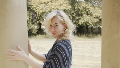 in slow motion, a young blonde woman flirts with the camera as it follows her around concrete temple pillars