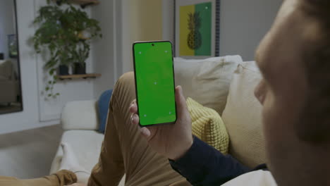 digital interaction: person touches green screen smartphone on sofa