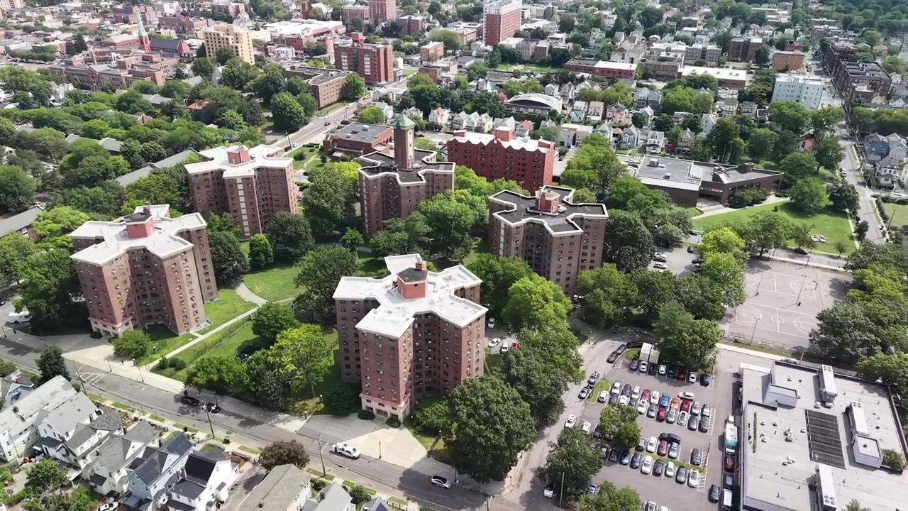 Vista aerea rotante di un grande complesso di edilizia popolare con edifici residenziali in mattoni circondati da alberi verdi e parcheggi in un denso quartiere residenziale urbano in una giornata di sole.