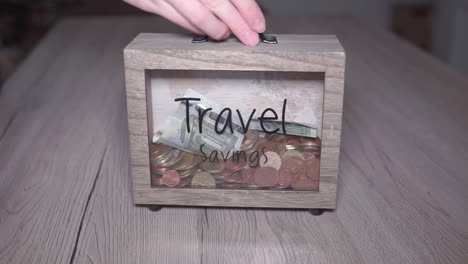 close up shot of a hand putting money in a wooden box for travel savings