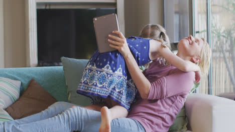 Vista-Lateral-De-Una-Mujer-Caucásica-Usando-Una-Tableta-Digital-Y-Jugando-Con-Su-Hija-En-Casa