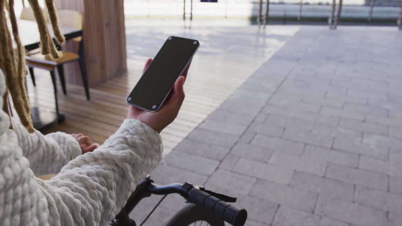 Mixed race man with dreadlocks wheeling bicycle in the street using smartphone