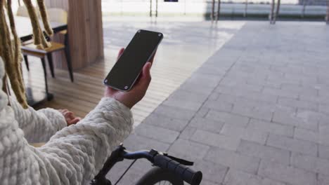 Mixed-race-man-with-dreadlocks-wheeling-bicycle-in-the-street-using-smartphone